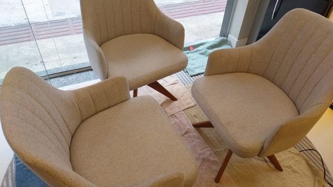 Três poltronas giratórias de tecido bege apoiadas sobre panos de secagem, em frente à vitrine de vidro de um ambiente comercial